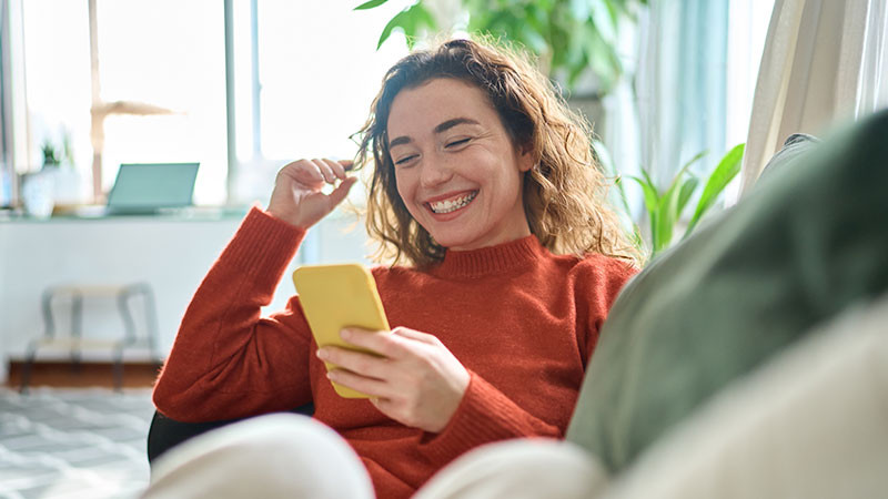 Image of a woman sitting down and smiling while looking at a cell phone